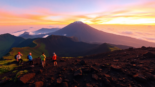 Hikers viewing Mount Rinjani at sunrise from the crater rim with vibrant sky and lush landscape